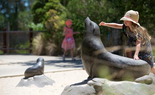 Young guest reaching for a Seal sculpture's raised head, with another pacing right in the background.