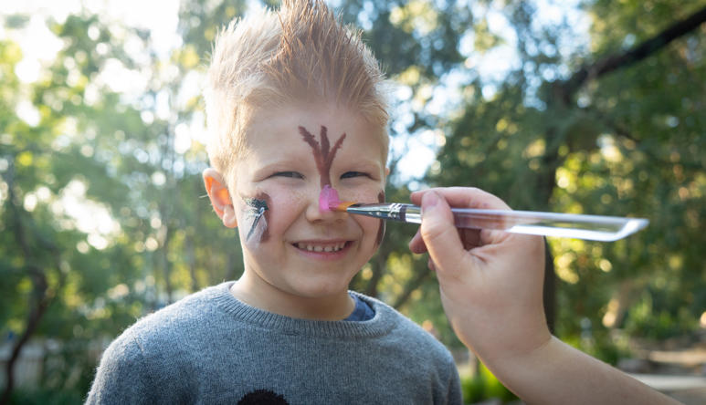 A young guest, grinning while having his face painted, as part of Possum Play Thursday.