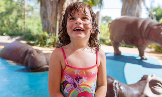 A young girl in bathers is smiling. There are fake hippo statues in the background.