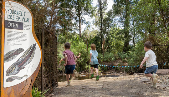 Three young guests running back towards the shallow Creek of Poorneet Creek Play, with its sign on the left.