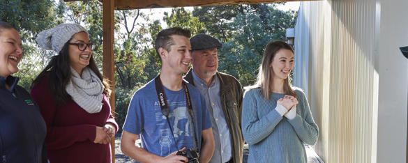 Two zoo keepers stand with a group of four adults who are all grinning.