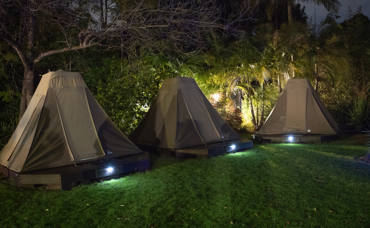 Three closed Roar 'n' Snore tents at night, with small lights around them.