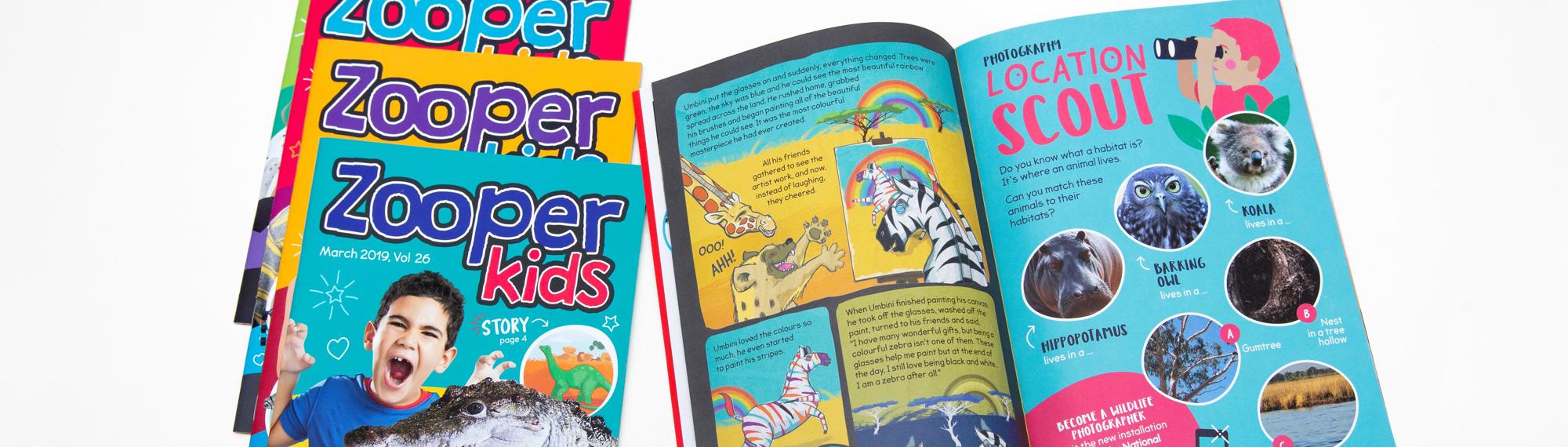 Five Zooper Kids magazines, four in a slanted stack on the left, one open on the right.