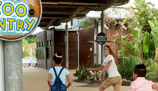 Three kids running past a sign that says Zoo Entry