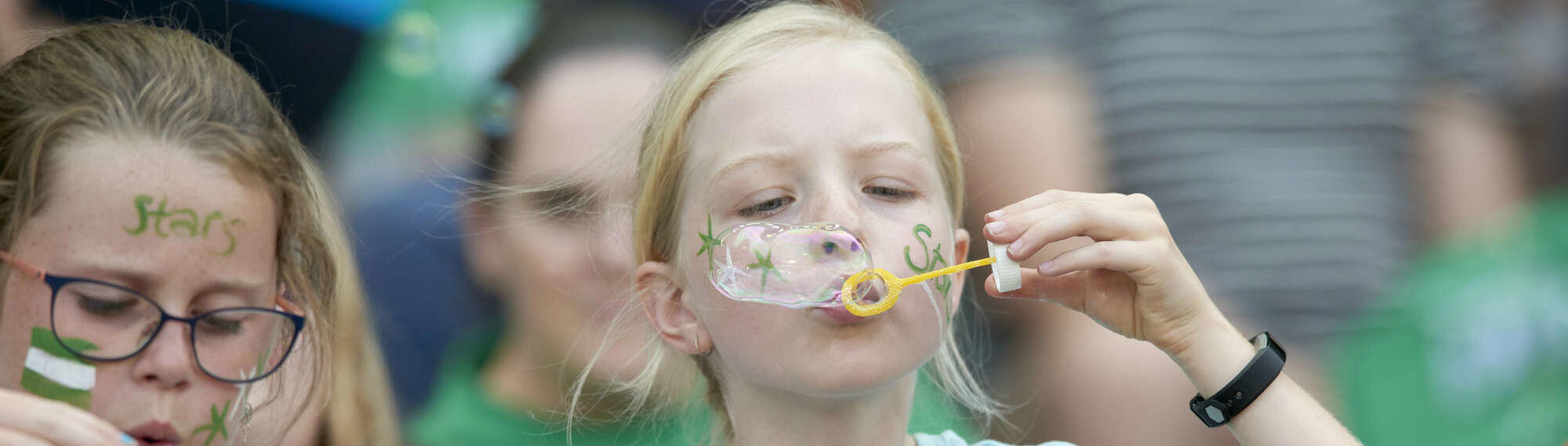 Young girl blowing bubbles with bubble wand at large event.