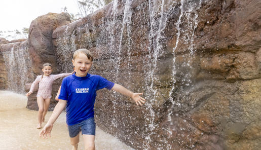 Three young guests run past a small waterfall, running towards and smiling to the camera.