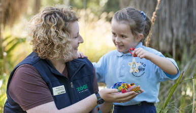 A Student with a ZV Educator, holding up her Beads for Wildlife craft creation.