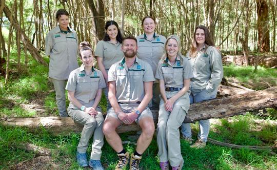 A group of zoo employees sit and stand in a group while smiling