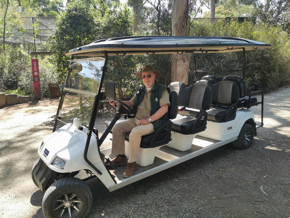 A volunteer rides on a buggy along a track in Healesville Sanctuary, he is smiling at the camera