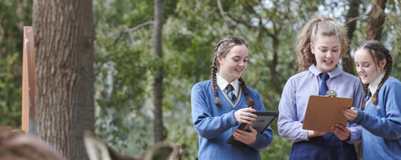 Three secondary school girls in blue uniforms smile as they look at two clipboards