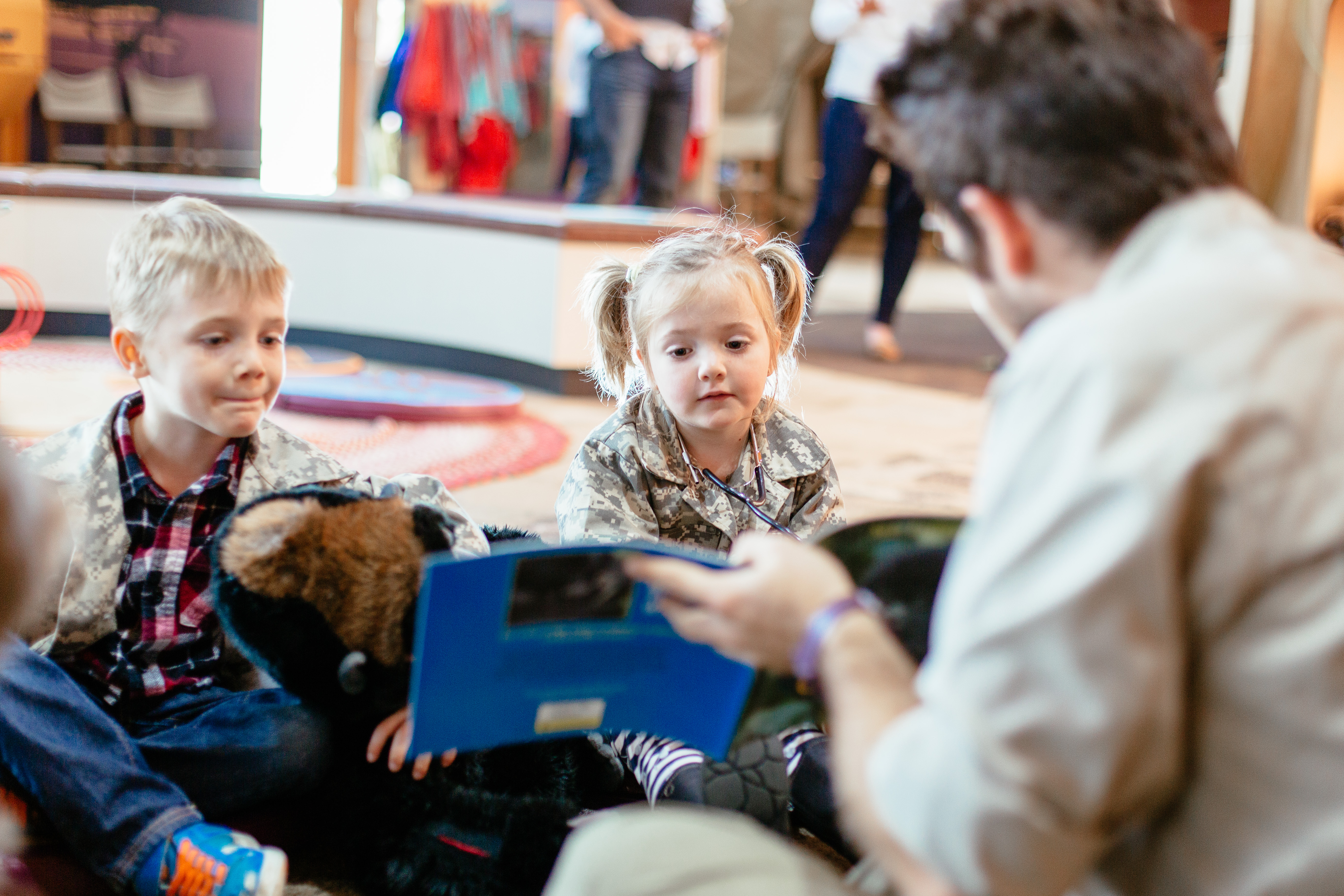 At least two young guests at Keeper Kids, being shown a story-book by a hosting Keeper.