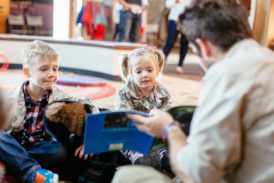 At least two young guests at Keeper Kids, being shown a story-book by a hosting Keeper.