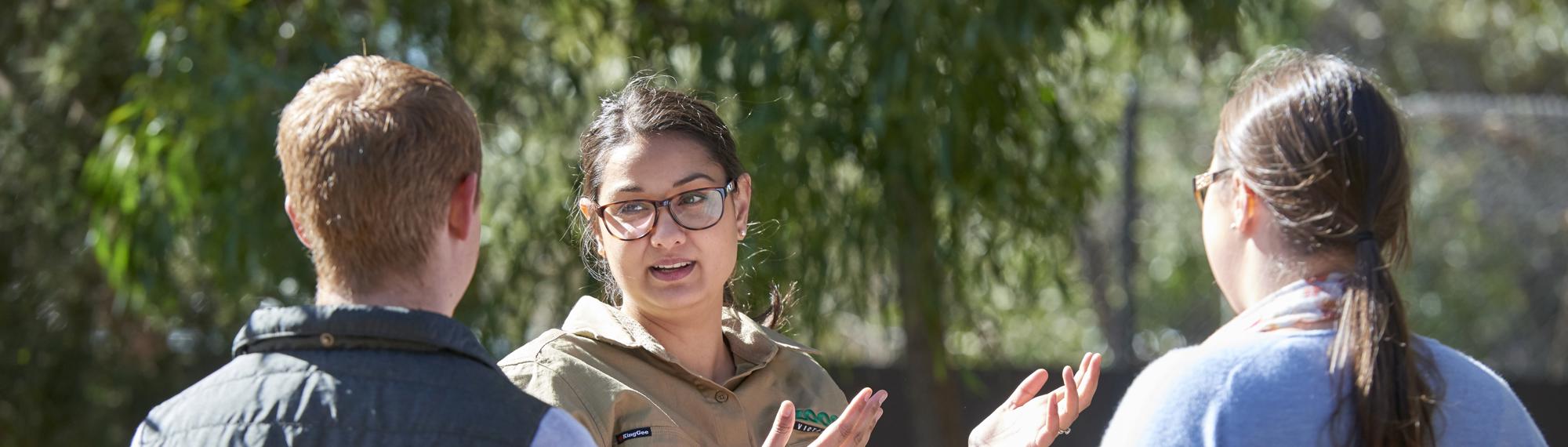 Keeper stands in front of two students (seen from behind) amid conversation.