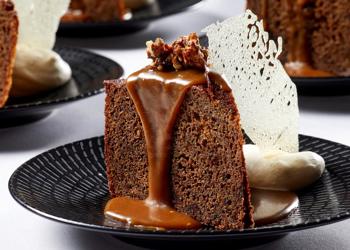 Close-up of a dessert cake with chocolate sauce, cream and wafer, on a table with at least three identical dishes.
