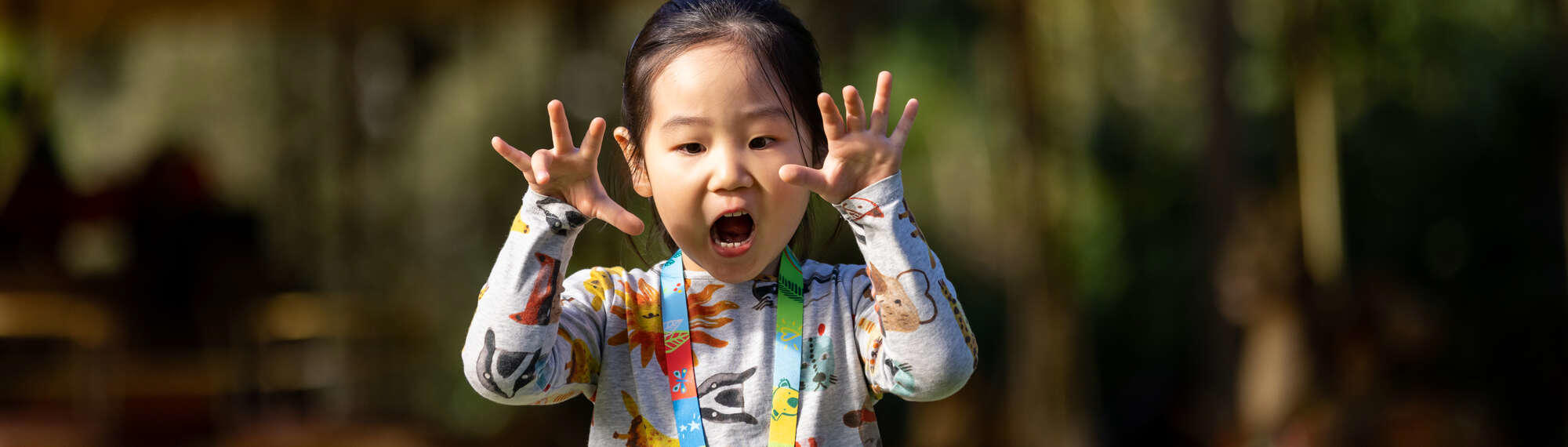 A girl playfully roaring at the camera with her hands raised, with the Carousel in the background.