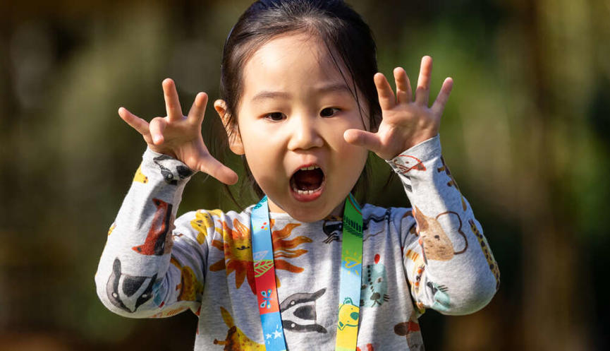 A girl playfully roaring at the camera with her hands raised, with the Carousel in the background.