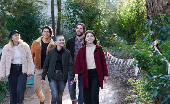 Five visitors walking towards the camera. Beautiful bushland background, gum trees and event bunting are also in the frame.
