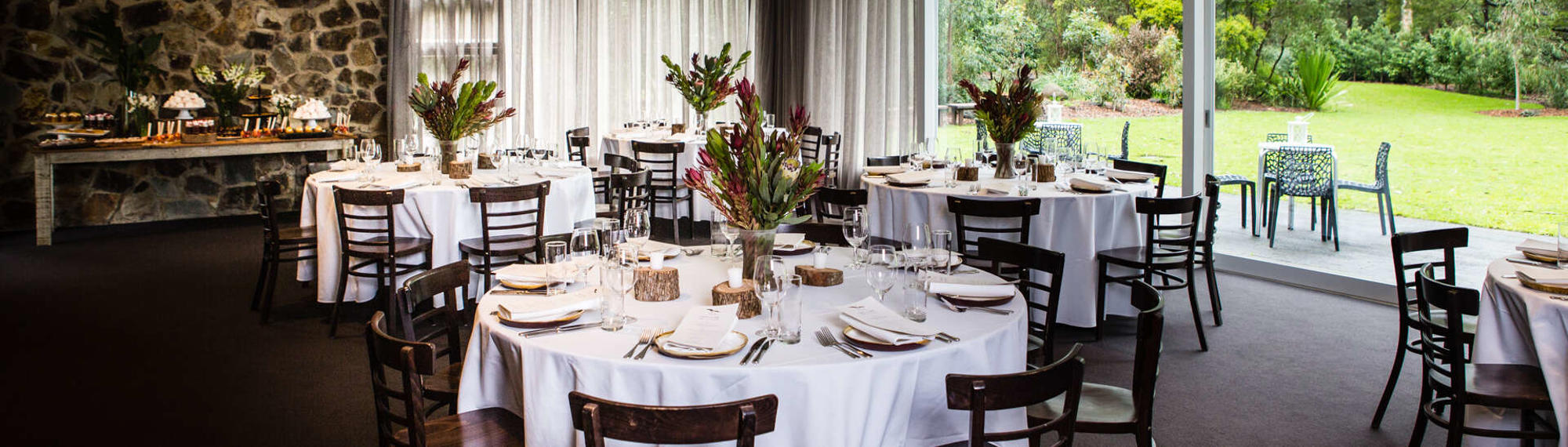 The Brogla room, set up with five dining tables, eight chairs per tables, a long table with snacks and flowers on it and two outdoor tables with four chairs each.