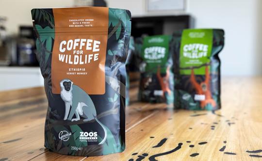 Three bags of coffee on a wooden table, all with the label "Coffee for Wildlife" and each with a different illustration of an animal; the bag in the foreground features a monkey.