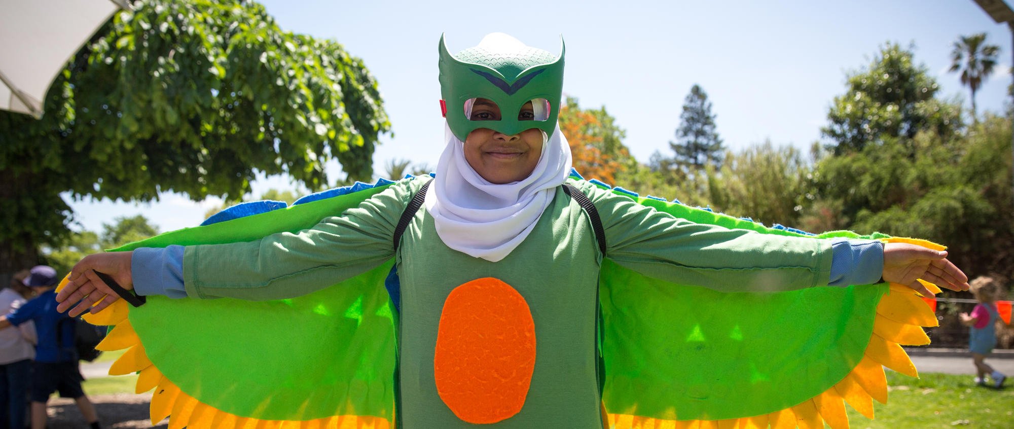 Student wearing Orange-bellied Parrot themed costume, with her arms (wings) outstretched.
