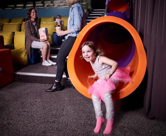 A girl sliding down the orange V-Junior slide, in the company of at least three other guests.