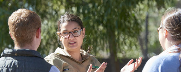 A zoo keeper stands in front of two high school ages children in conversation.