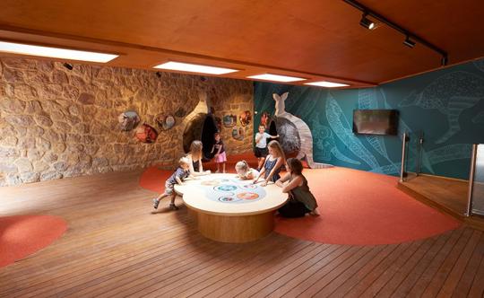 View of inside Pouch House, with eight guests gathered around the central activity table.