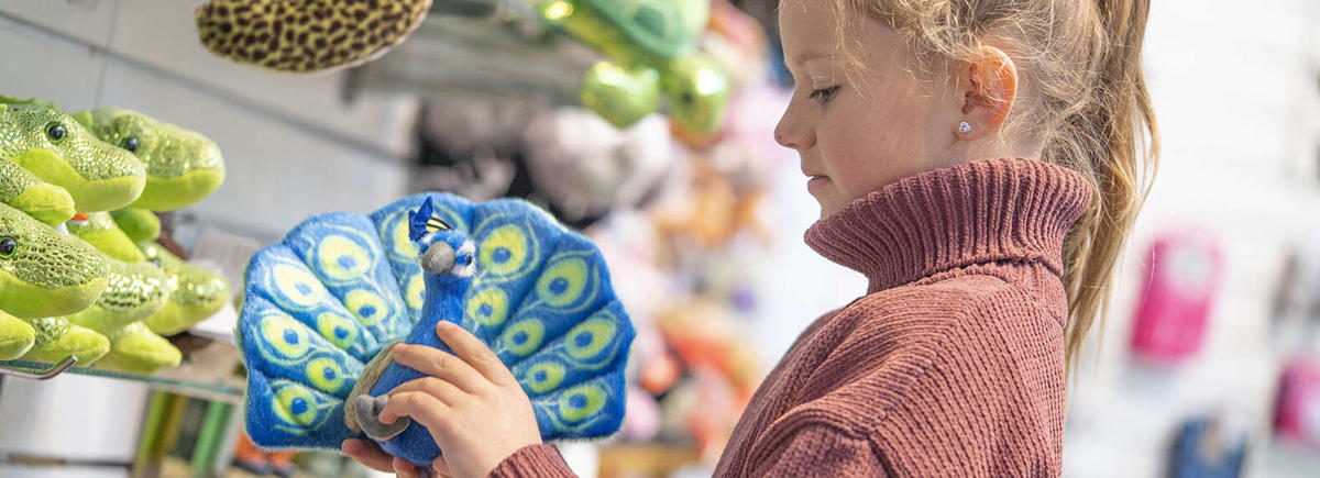 A girl looking (left) at a plush Peacock, one of the toys at the Zoo Shop.