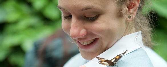 A secondary student smiles as she looks at a butterfly on her shoulder.