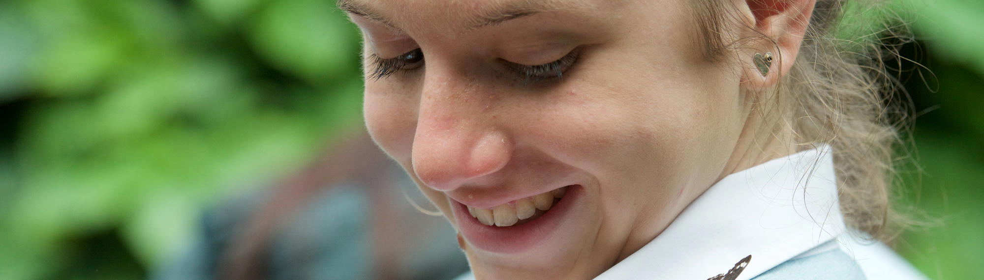 A secondary student smiles as she looks at a Monarch Butterfly on her left shoulder.