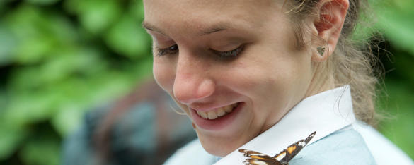 A secondary student smiles as she looks at a Monarch Butterfly on her left shoulder.