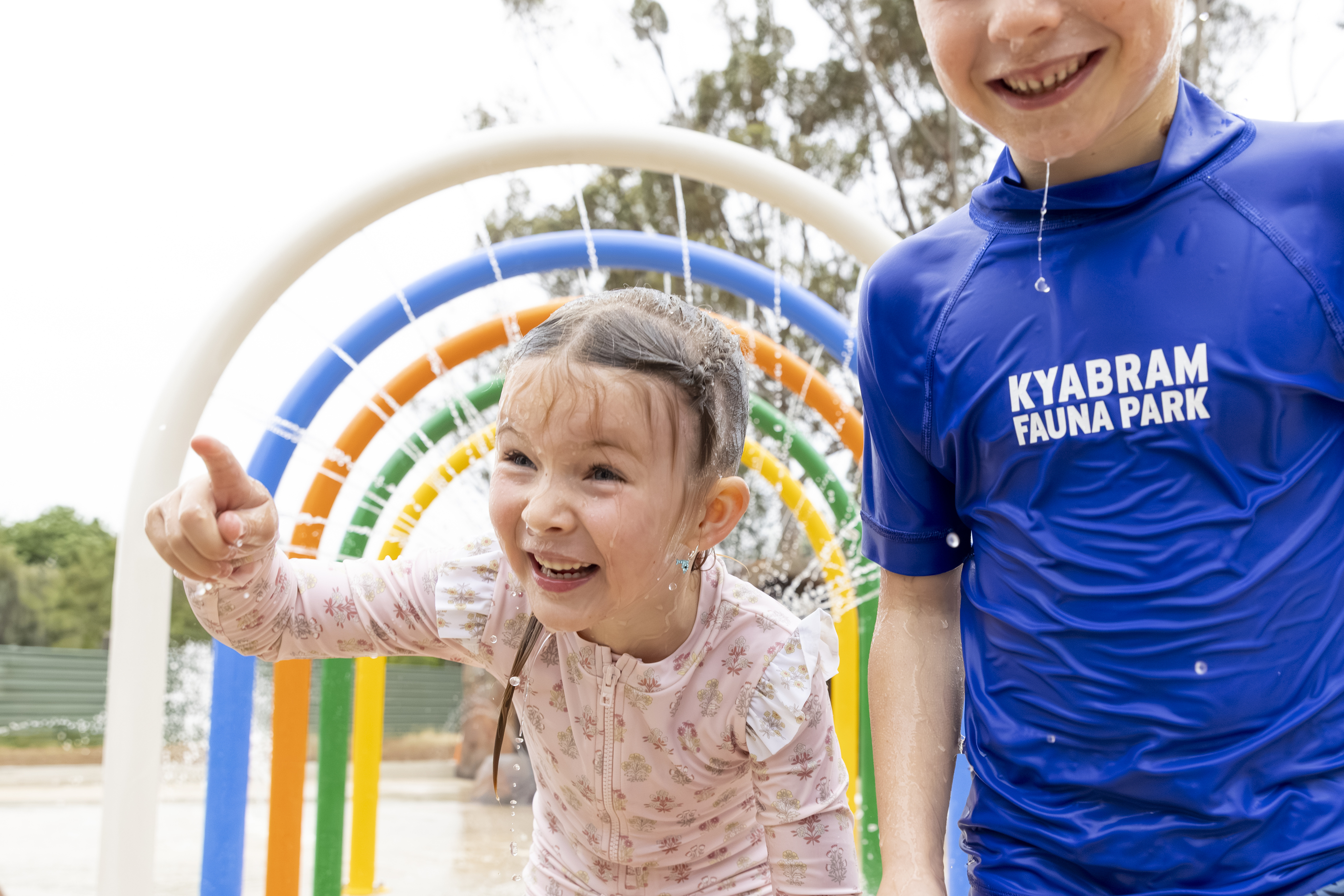 Two young guests enjoying the Splash Park's water arches, one pointing left of frame.