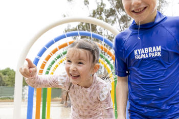 Two young guests enjoying the Splash Park's water arches, one pointing left of frame.