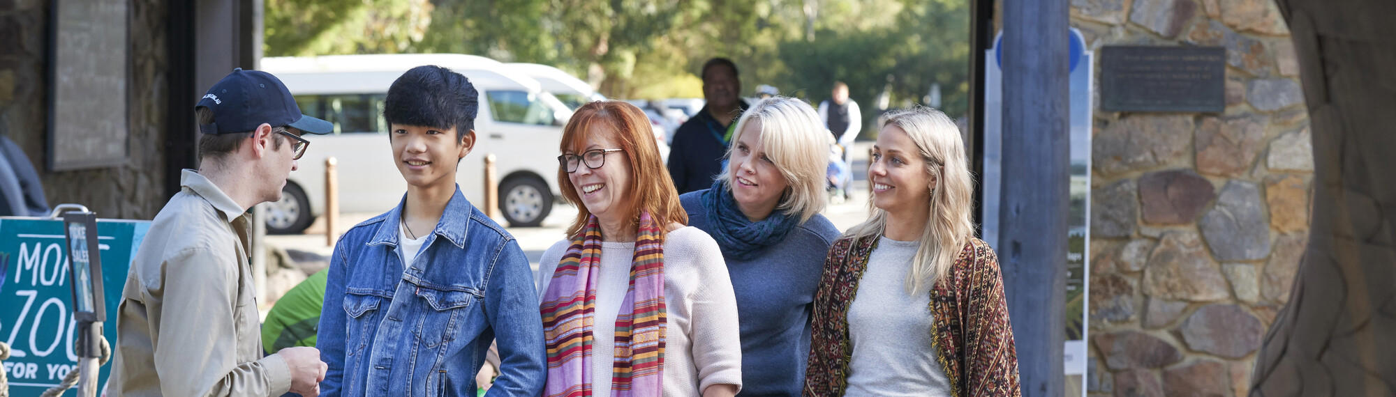 A Zoo member of staff (in khaki uniform) greets four people as they enter through Healesville Sanctuary's entrance.