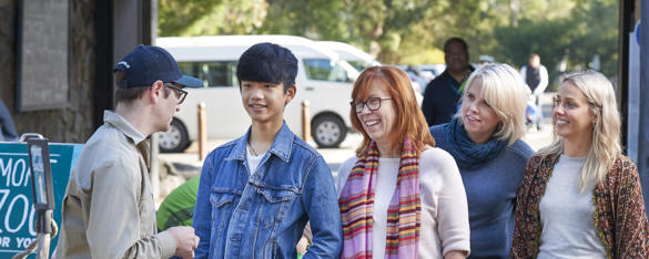 A Zoo member of staff (in khaki uniform) greets four people as they enter through Healesville Sanctuary's entrance.
