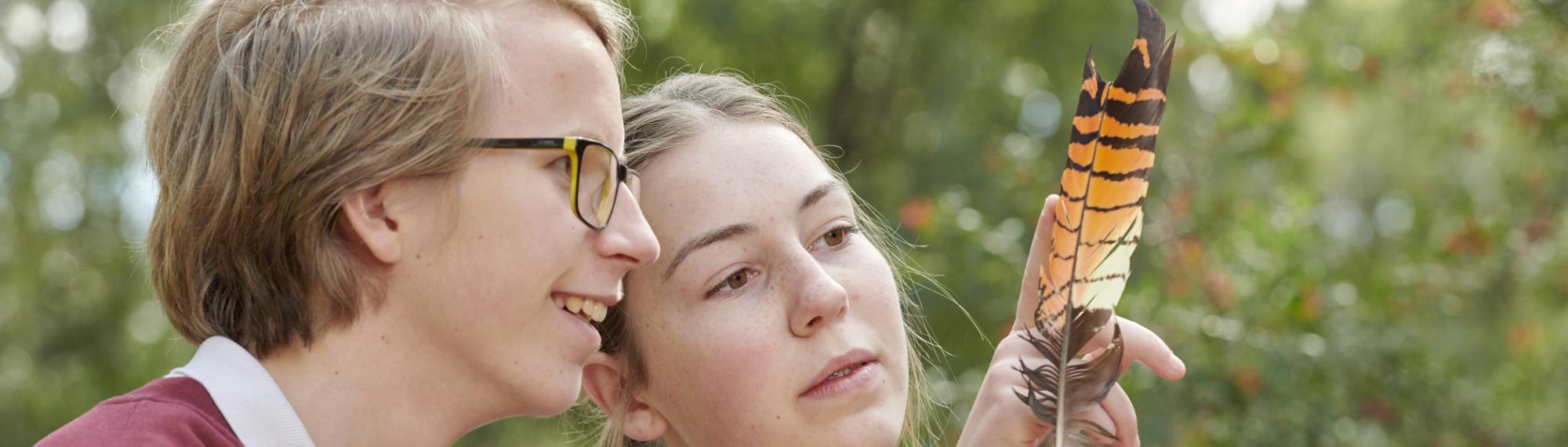 Two students examining an orange-and-brown-striped bird's feather, facing right.