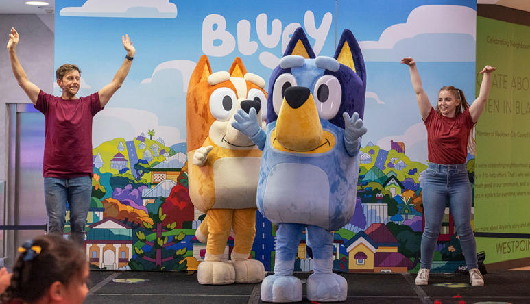 Bluey and Bingo mascots on stage with two performers standing with their arms up