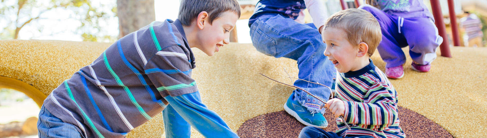 Two kids playing in the Village Kids playground, one holding a stick.