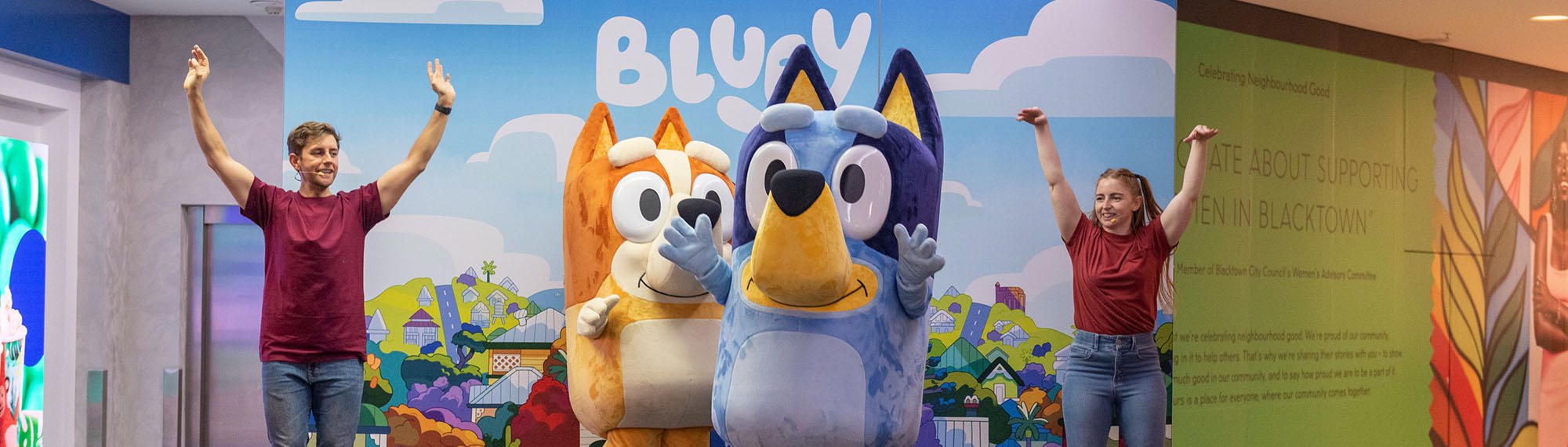 Bluey and Bingo mascots on stage with two performers on either side of them, all standing with their arms up.