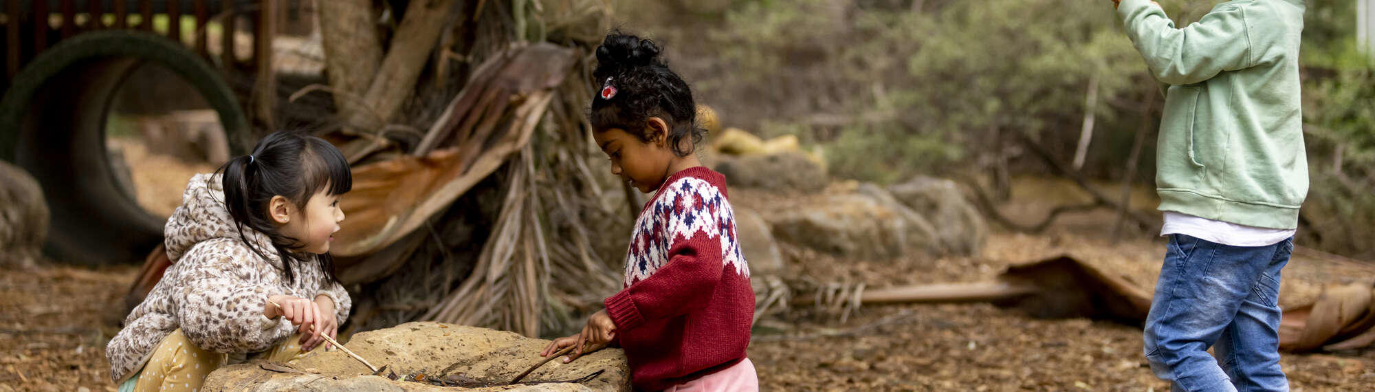 Two children playing with sticks and rocks in an outdoor playground