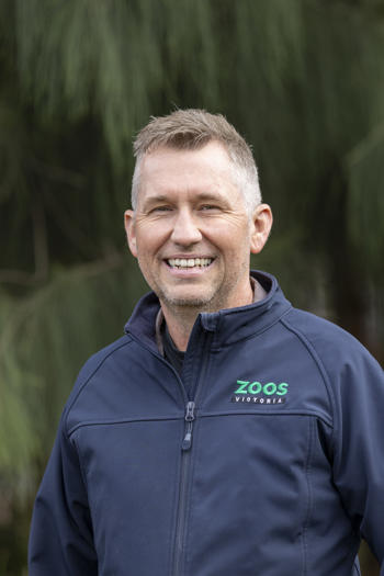 Portrait of Vet Garry, in front of a leafy backdrop.