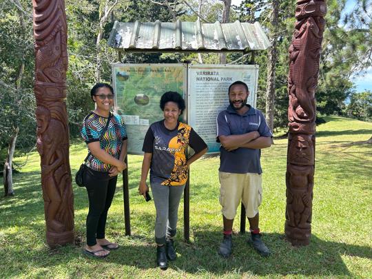 Three Papuans posing in front of a map-sign for Varirata National Park.