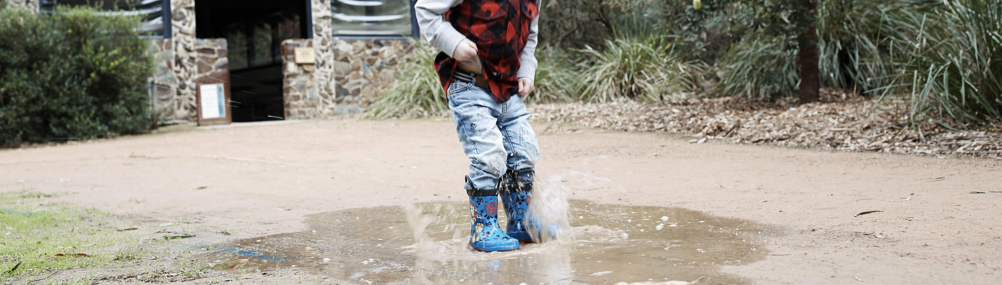 A boy wearing blue gumboots in a puddle