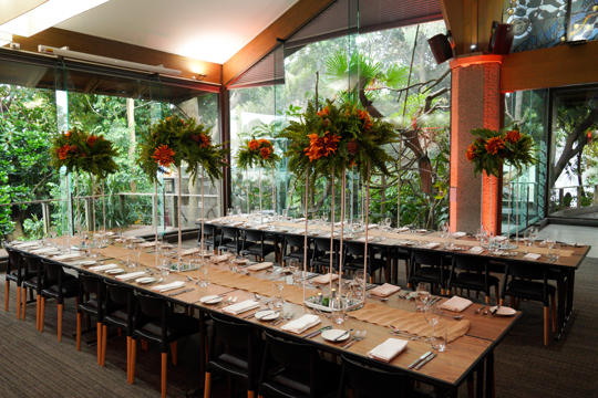View of the Rainforest Room, prepped for a ceremony with flowers, tables and chairs .