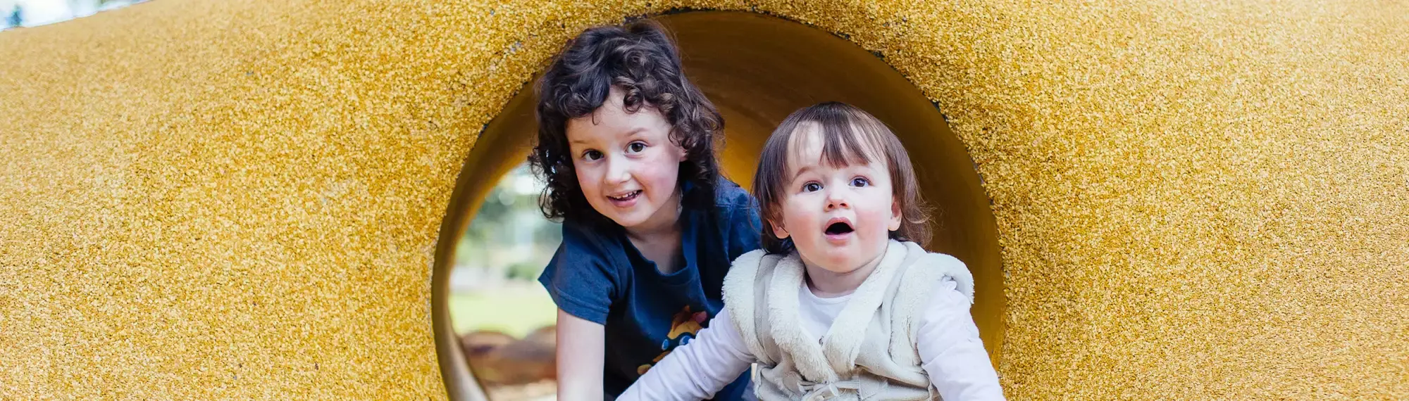 Two children crawling in a yellow tunnel, looking at the camera.