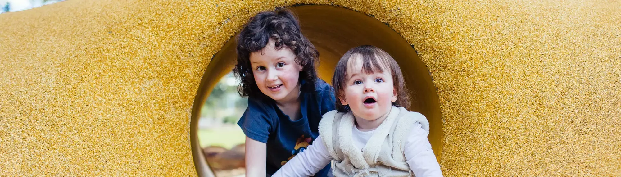Two children crawling in a yellow tunnel, looking toward the camera.