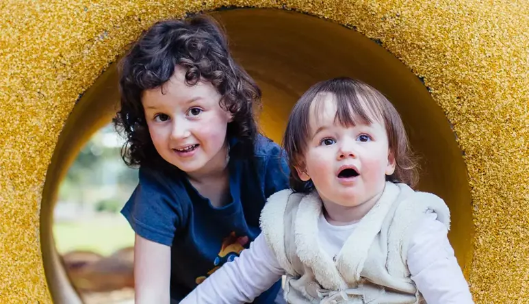 Two children crawling in a yellow tunnel, looking toward the camera.