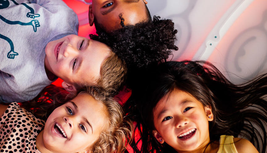Four young guests joyfully lying in a semi-circle group, on the light-up Dragon Disco floor.