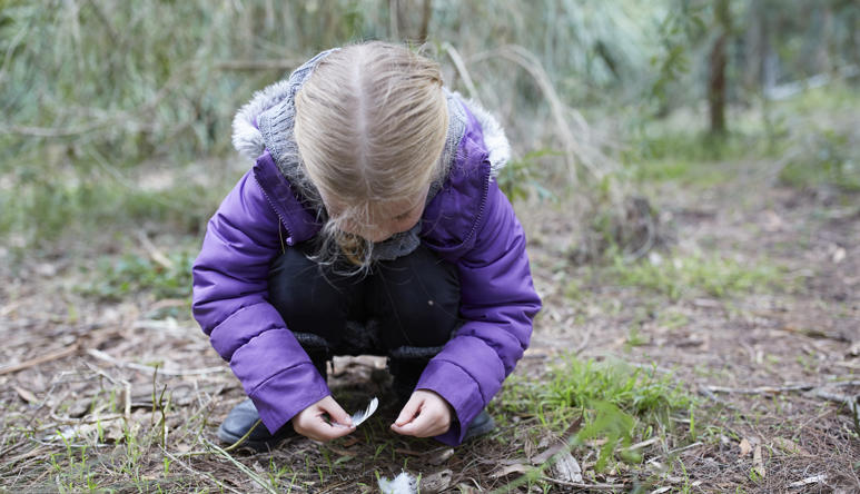 A young guest crouched down and picking up feathers from the ground.