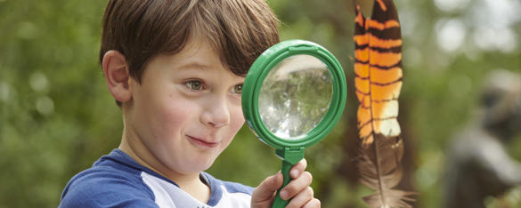 Kinder Keeper Kid examines a brown-and-orange feather with a green magnifying glass.